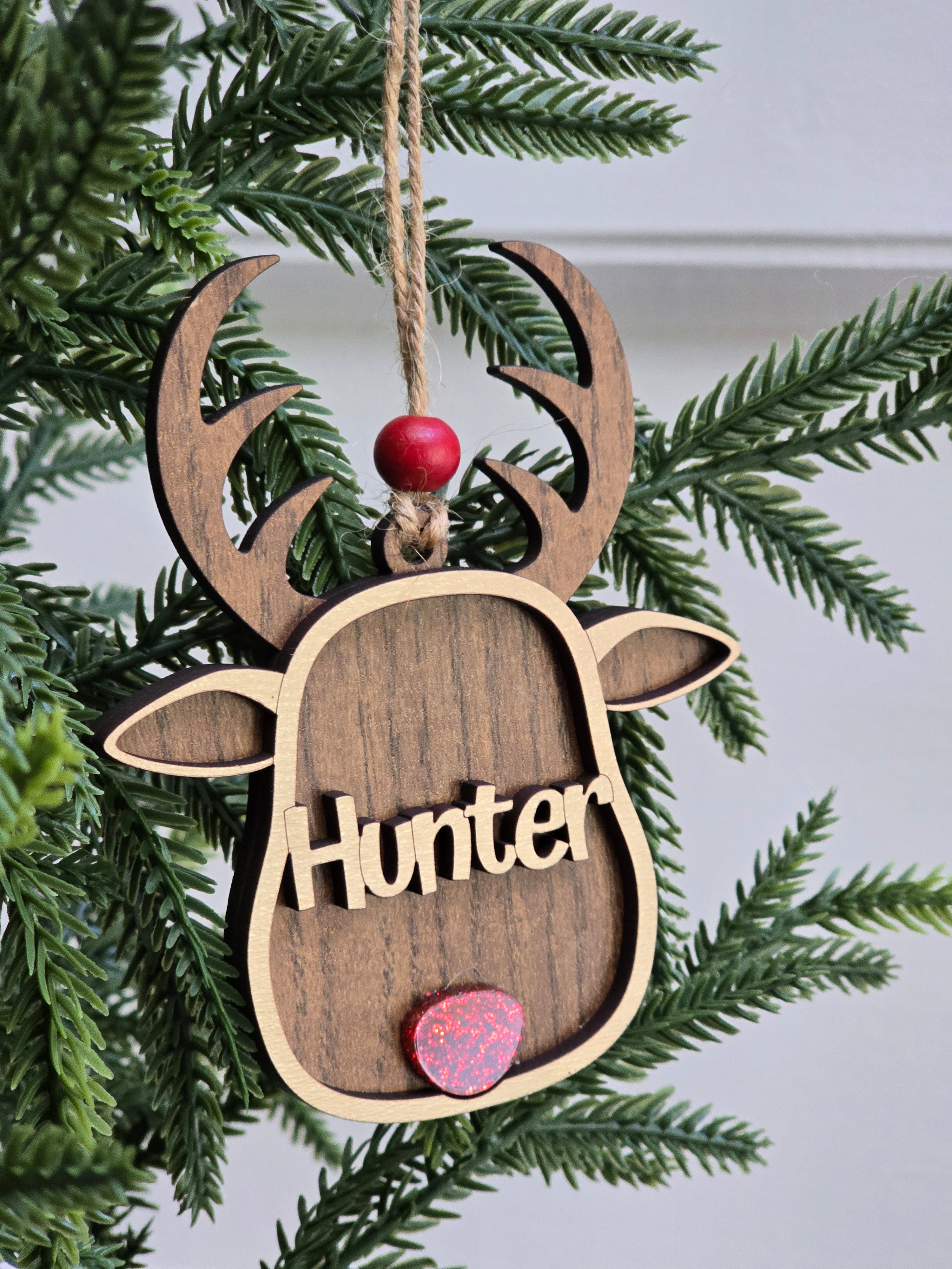 Wooden ornament shaped like a deer head with 'Hunter' engraved, hanging on a Christmas tree.