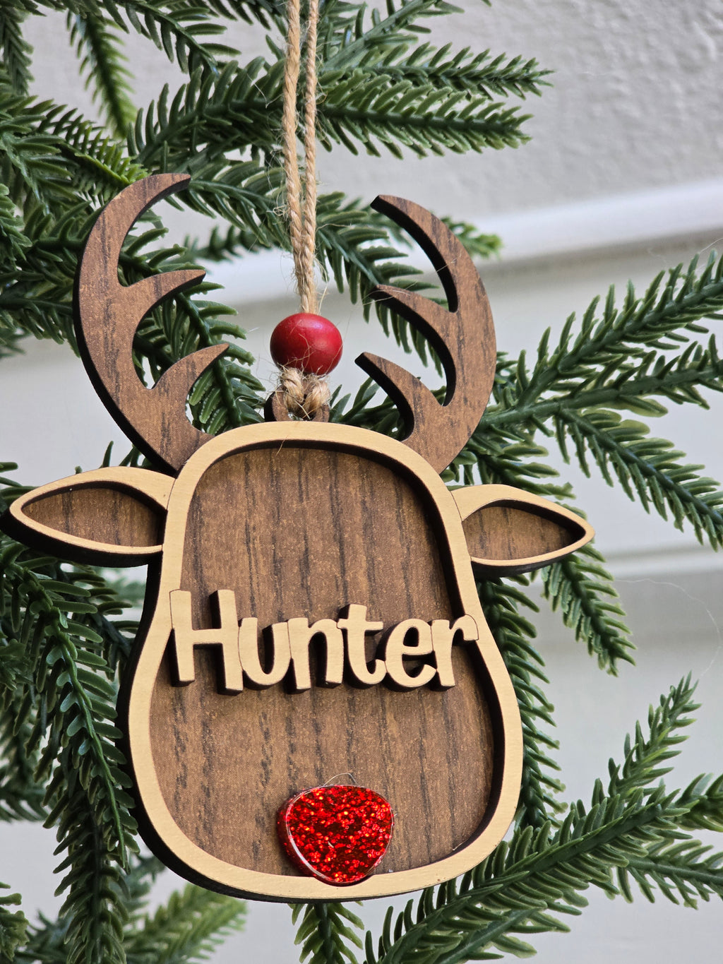 Wooden ornament shaped like a dog tag with 'Hunter' engraved, attached to a Christmas tree.