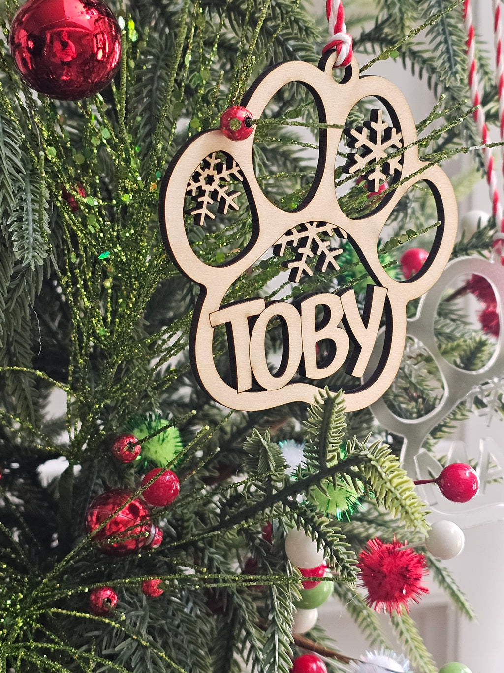 Wooden ornament with 'Toby' on a Christmas tree with red berries and green leaves.