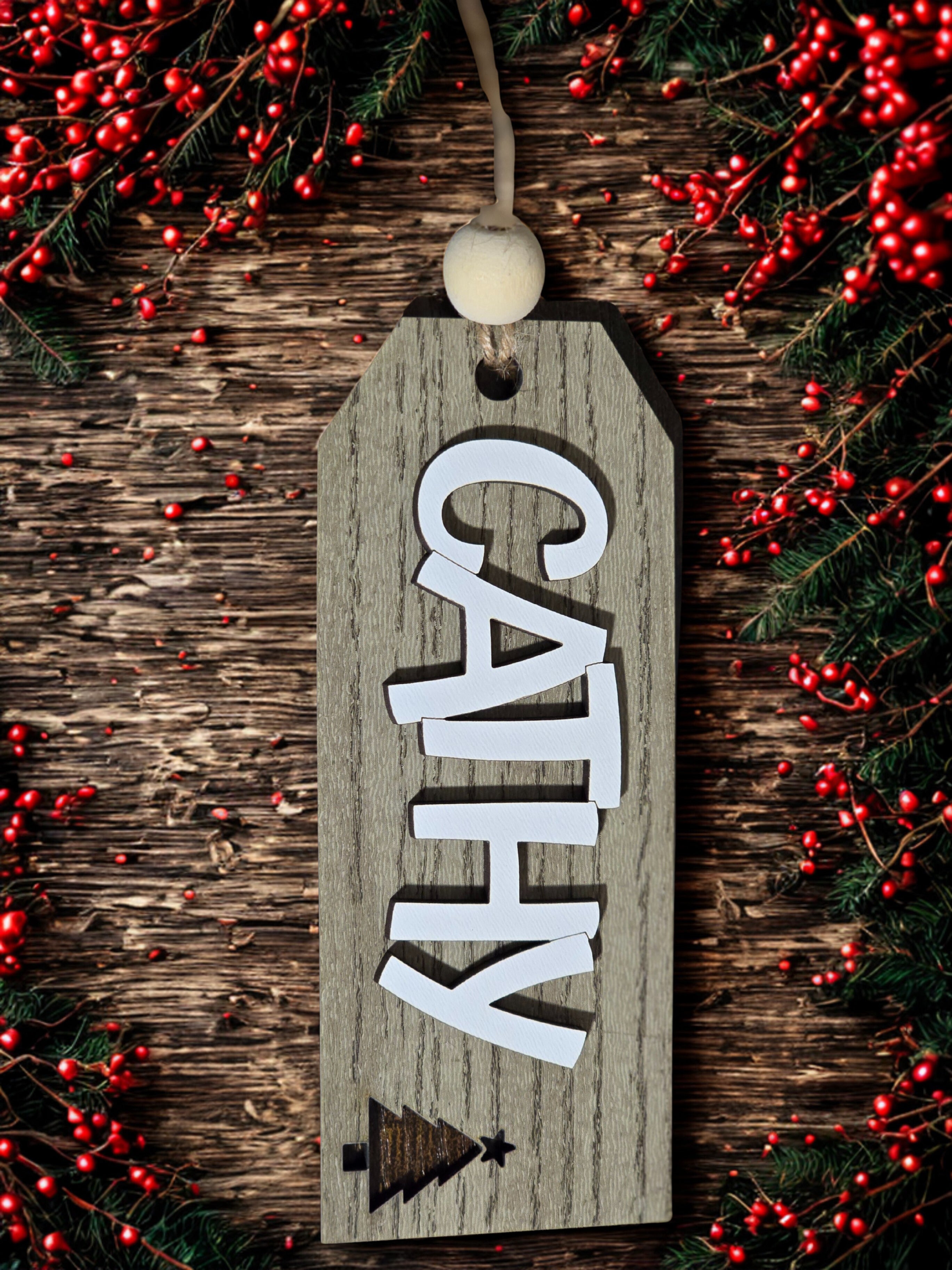 Wooden tag with 'CATHY' on a rustic wooden background with red berries and greenery.