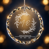 Personalized beveled glass Christmas ornament engraved with M + E, GREATHOUSE, and 10 · 03 · 26 against warm tree lights