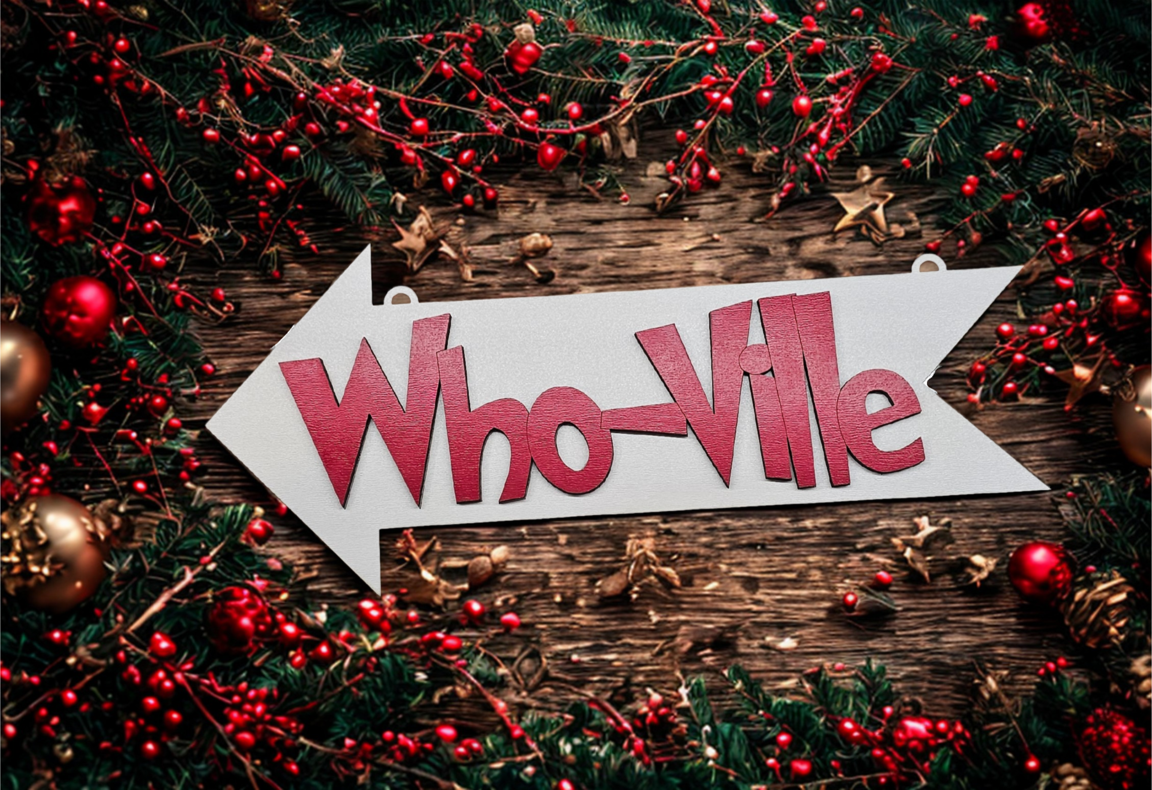 Decorative sign with 'Who-Ville' text surrounded by Christmas decorations on a wooden surface.