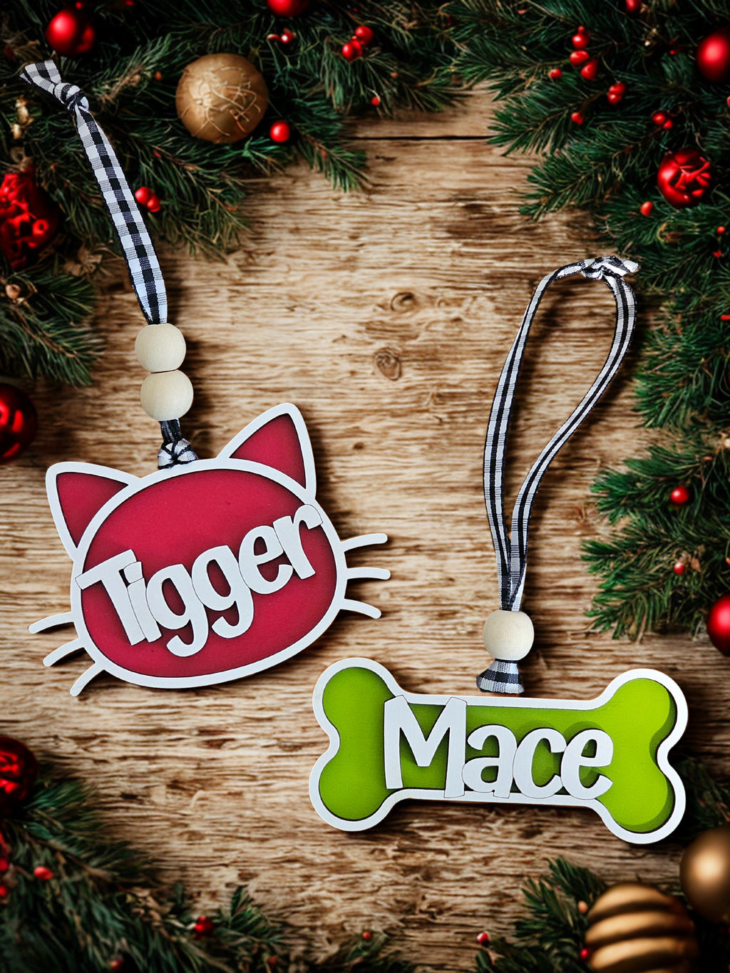 Two pet name tags, one red with a cat design and one green with a bone design, on a wooden surface with Christmas decorations.