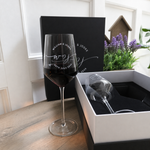 Engraved wine glass filled with red wine displayed beside the open gift box