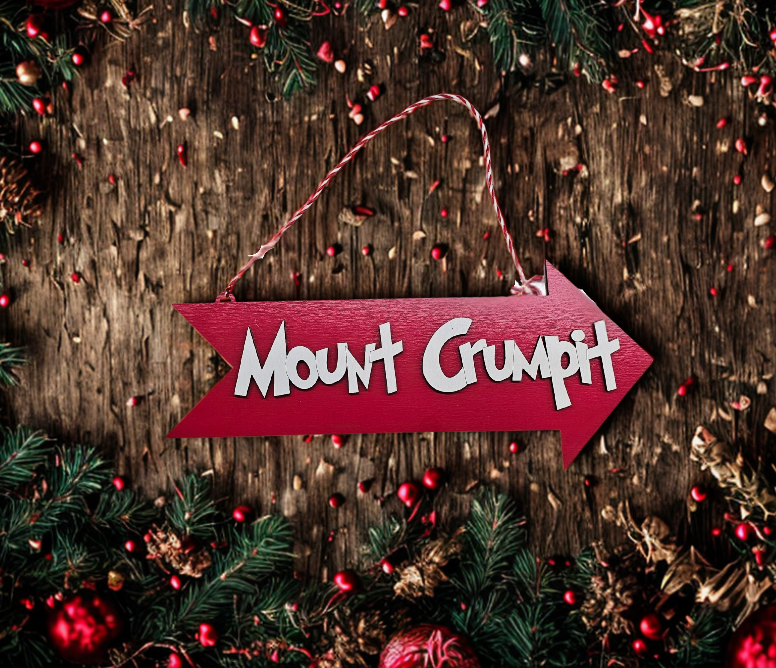 Red arrow-shaped sign with 'Mount Grumpit' text on a wooden background with Christmas decorations.