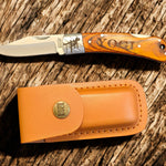 Lineman folding knife shown open with leather sheath on rustic wood background