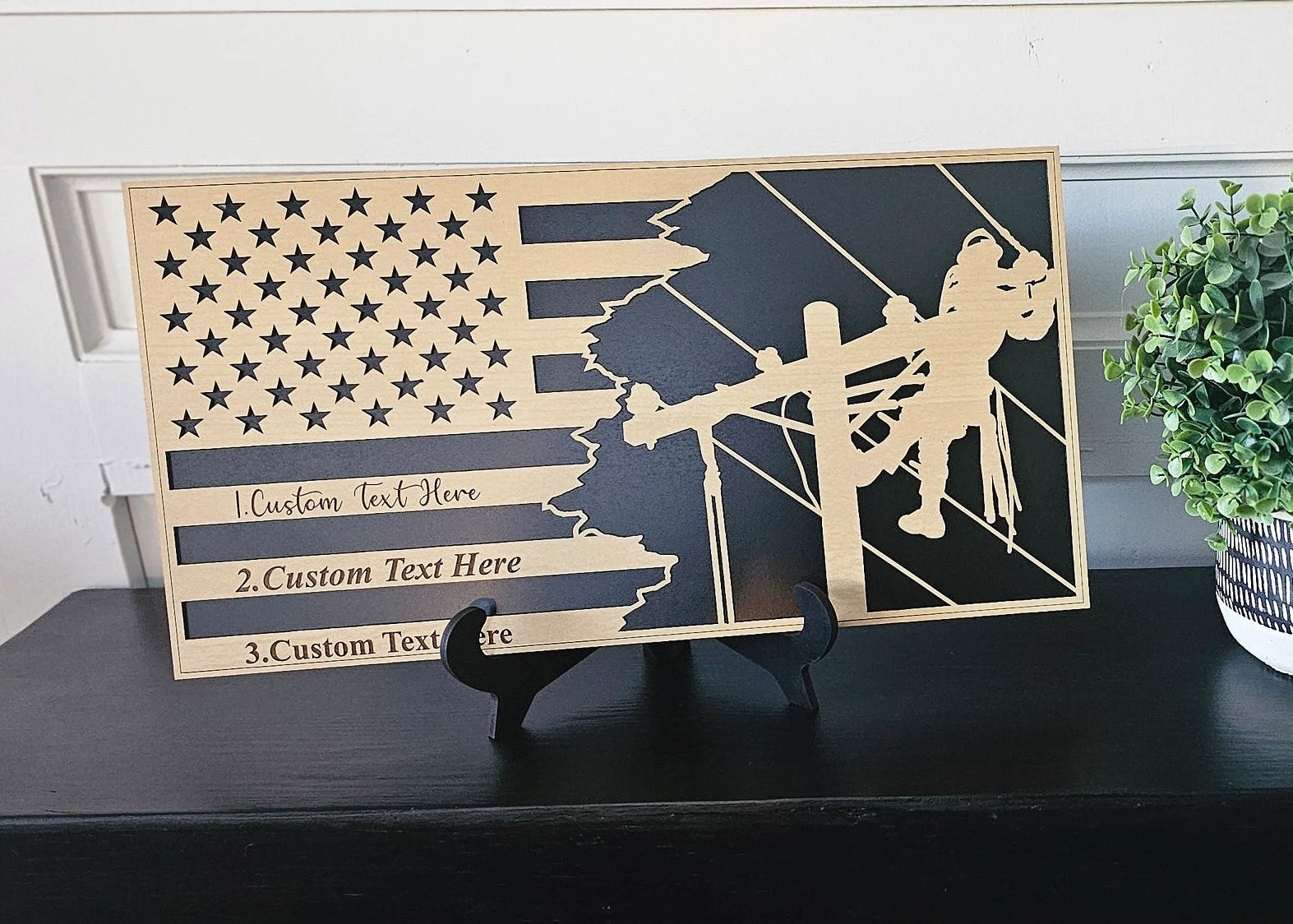 Personalized lineman flag plaque displayed on a black shelf with plant decor and included tabletop stand