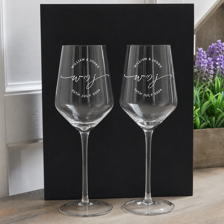 Pair of empty personalized wedding wine glasses displayed against a black background