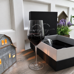 Personalized wine glass filled with red wine beside the open matching gift box