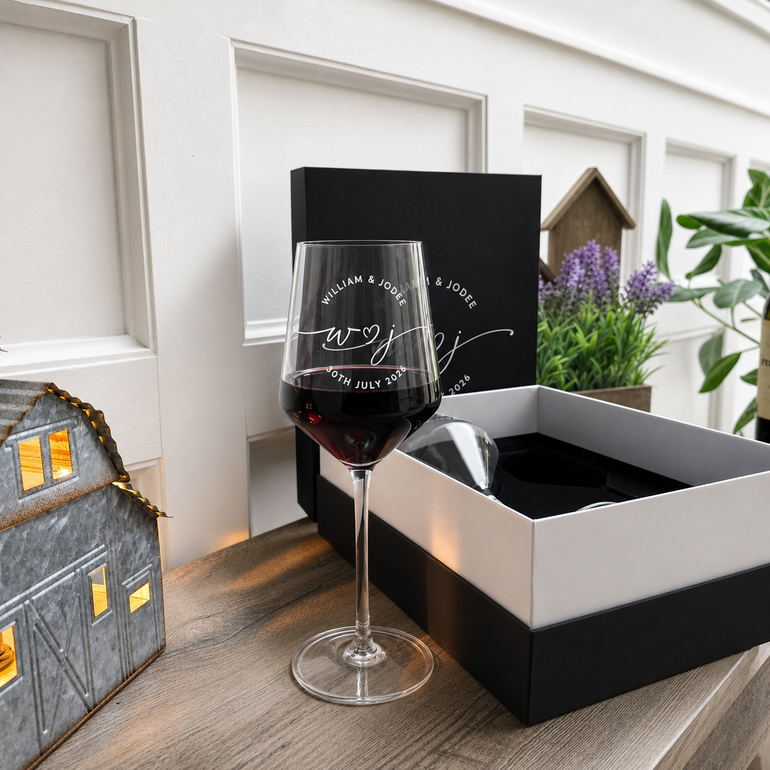 Personalized wine glass filled with red wine beside the open two-glass presentation box
